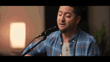 a man singing into a microphone wearing a blue plaid shirt