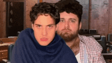 two men are sitting next to each other and one of them is wearing a blue blanket