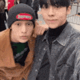 two young men are posing for a picture together while one of them is wearing a supreme hat .