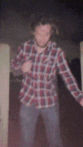a man wearing a plaid shirt is dancing in a dark room