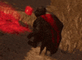 a man in a red cape is standing in front of a red flame .