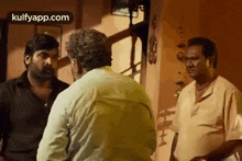 a group of men are standing next to each other in a room and talking .