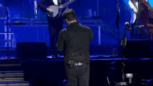 a man in a black shirt stands on a stage with a banjo player behind him