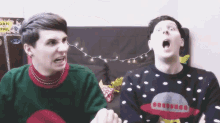two men wearing ugly christmas sweaters are sitting next to each other on a couch .