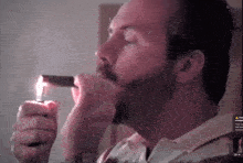 a man with a beard is lighting a cigar in front of a screen that says " i am "