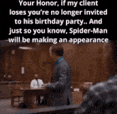 a man in a suit stands in a courtroom talking to a man in a blue shirt