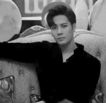 a black and white photo of a man sitting on a couch with balloons in the background .