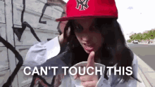 a woman wearing a red hat says " can 't touch this " in front of a graffiti wall