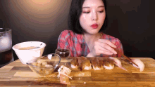 a woman is eating sushi on a wooden table with chopsticks