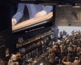 a large screen shows a man sitting at a bar with the words we are going to become freaks