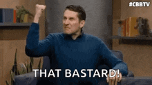 a man is sitting in a chair with his fist in the air and says `` that bastard ! ''