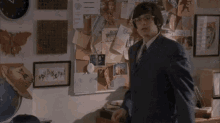 a man in a suit and tie is standing in a room with a bulletin board .