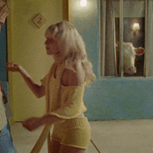 a woman in a yellow top and shorts stands in front of a door with a number 2 on it