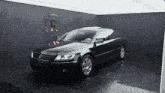 a black car is parked in front of a wall with a r on it