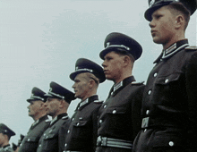 a group of soldiers are lined up in a row and one of them has the letter t on their hat