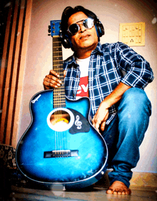 a man wearing headphones and sunglasses is kneeling down holding a blue guitar