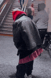 a person wearing a black leather jacket and a red hat is standing next to a staircase