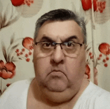 a man wearing glasses and a white shirt is making an angry face in front of a floral curtain .