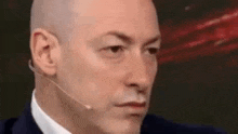 a bald man in a suit and tie is wearing a microphone on his head .