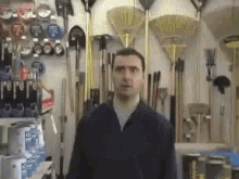 a man in a blue jacket is standing in front of a wall of tools including a broom
