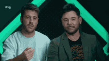 two men are sitting next to each other in front of a green background with rtve written on the bottom