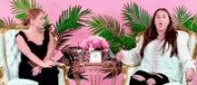 two women are sitting in chairs talking to each other in front of a table .