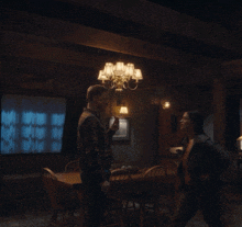 a man and woman are dancing in a dark room with a chandelier hanging from the ceiling