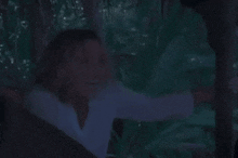 a woman in a white shirt is being held by a man in a white hat in a dark forest
