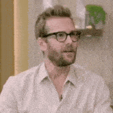 a man with a beard wearing glasses and a white shirt is making a funny face .