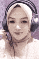 a woman wearing a hijab and headphones is smiling and looking at the camera .