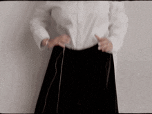 a woman wearing a white shirt and a black skirt is tying her skirt .