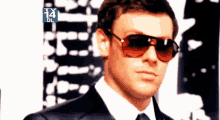 a man wearing sunglasses is standing in front of a tv screen that says ' tx 14 dl '