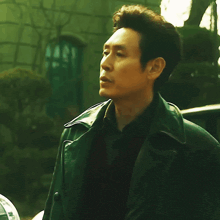 a man wearing a black leather jacket stands in front of a sign that says ' korean ' on it