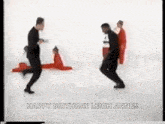 a group of men are dancing in front of a white background and a woman is laying on the floor .