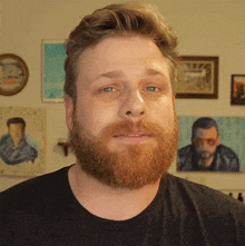 a man with a beard wearing a black shirt stands in front of paintings