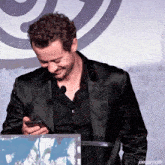 a man in a black suit is smiling while looking at his phone with the caption joequinngifs