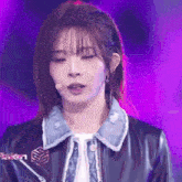 a woman wearing a black leather jacket and a denim jacket is standing in front of a microphone .