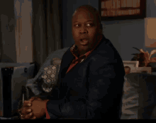 a man in a blue suit is sitting on a couch with his hands folded