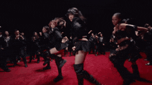 a group of women are dancing on a red carpet in a dark room
