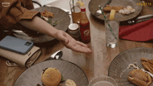 a woman reaches for a bottle of harlem hot sauce on a table