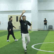 a man in a black shirt and white pants stands on a soccer field waving his hand