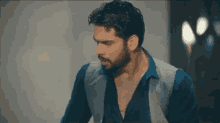 a man with a beard wearing a blue shirt and a gray vest is standing in a room .