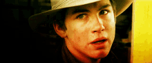 a young man wearing a cowboy hat looks at the camera with a surprised look on his face