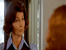 a woman wearing a striped shirt and a vest looks at another woman