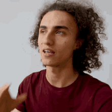 a young man with curly hair is wearing a red shirt
