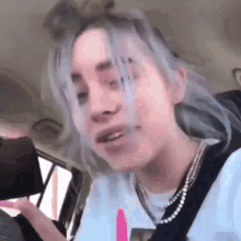 billie eilish is sitting in the back seat of a car with her eyes closed .