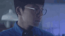 a close up of a man wearing glasses and a blue shirt in a dark room .