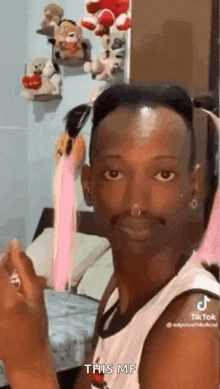 a man with a nose ring is standing in front of a bed holding a pink ribbon .
