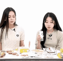 two girls are sitting at a table with food and one has a shirt that says bitch on it