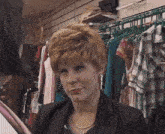 a woman in a black jacket is standing in front of a rack of clothes